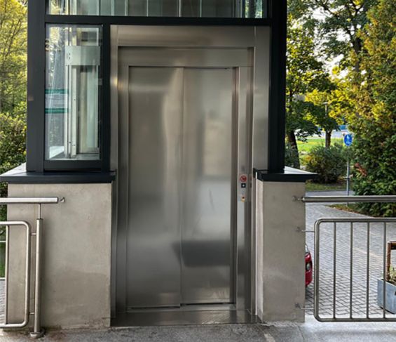 Edelstahltür des Aufzugs in einem verglasten Aufzugsschacht.